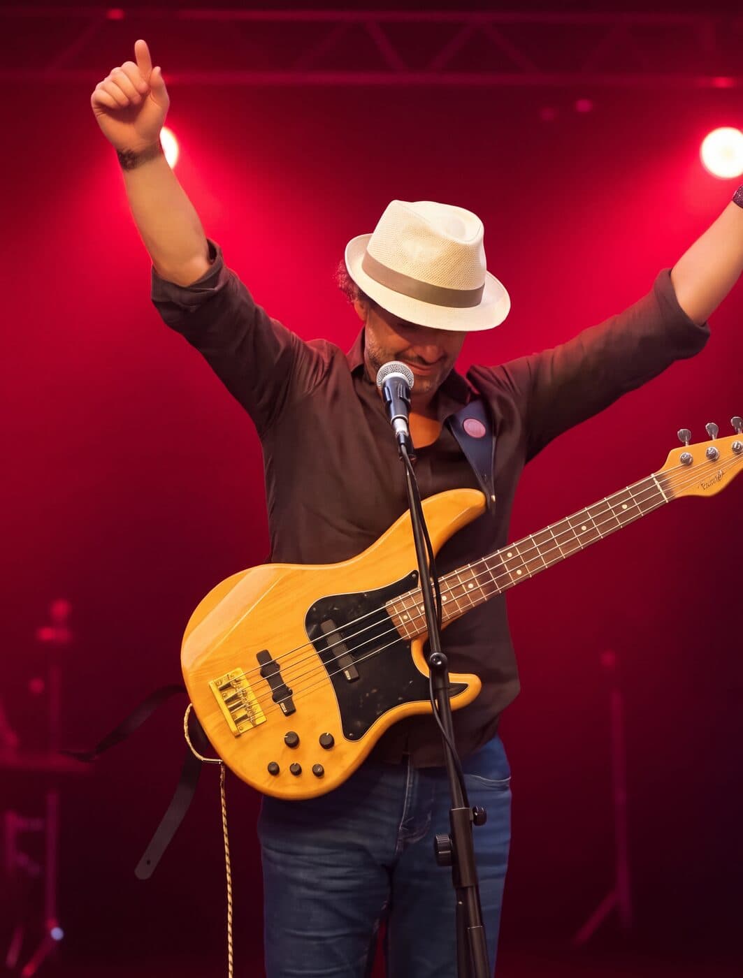 Osman Meyredi with his bass guitar, arms raised on a red-lit stage
