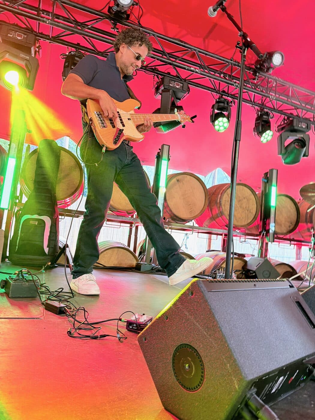 Osman Meyredi playing bass guitar on a festival stage lined with wine barrels