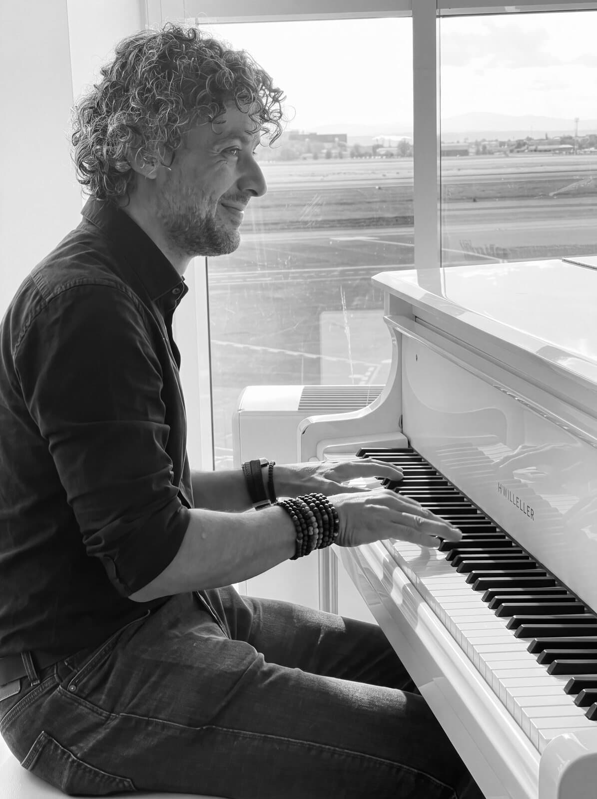 Osman Meyredi at a white grand piano by the window, black and white